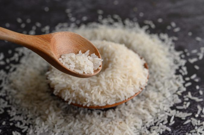 Milled rice in a bowl and a wooden spoon on the black cement floor. Selective focus
